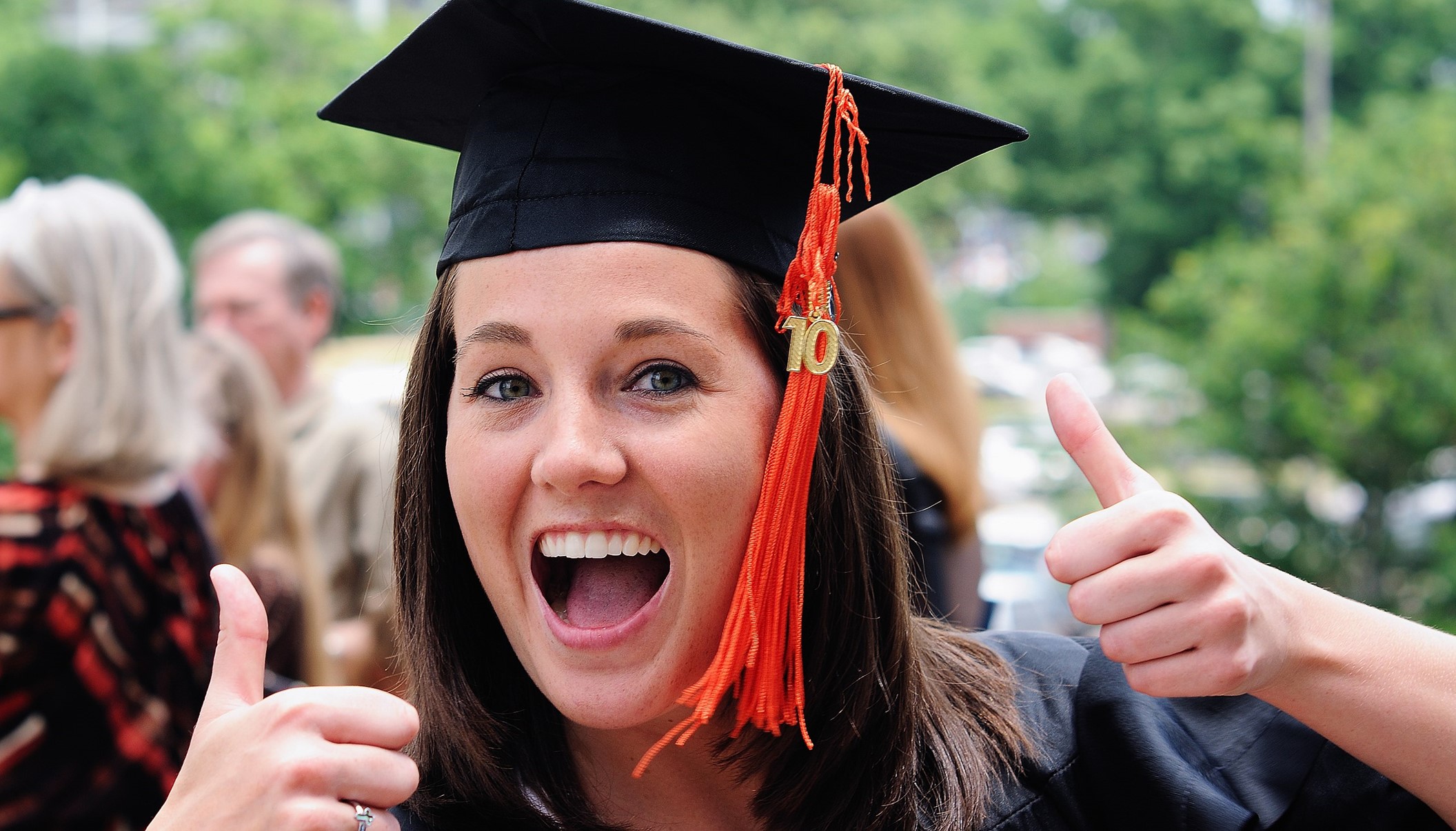 A new graduate indicates success with two thumbs up