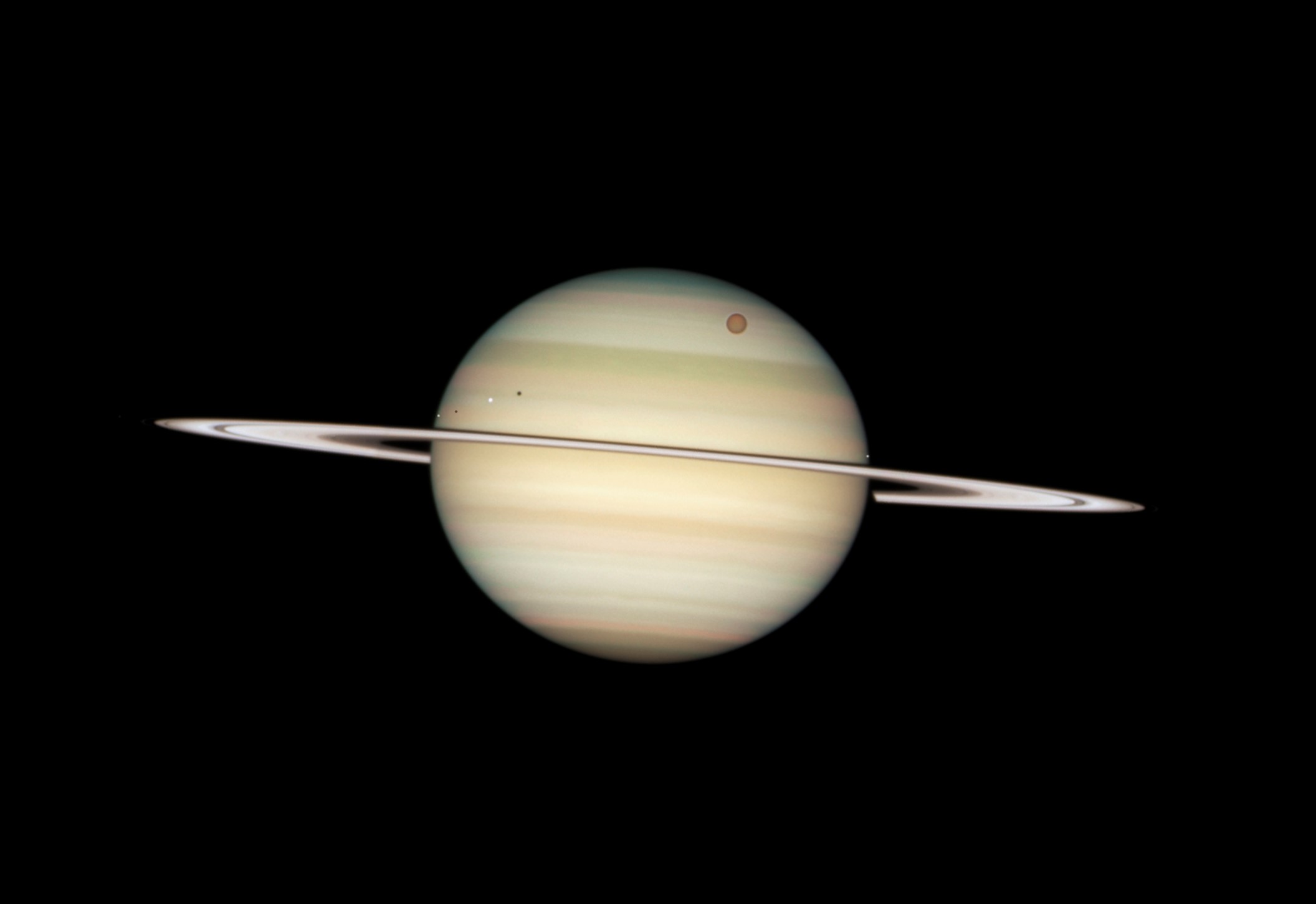 NASA/ESA Hubble Space Telescope captured a photo sequence of four moons of Saturn passing in front of their parent planet. The moons, from far left to right, are the white icy moons Enceladus and Dione (each preceded by their own shadow), the large orange moon Titan, and icy Mimas.